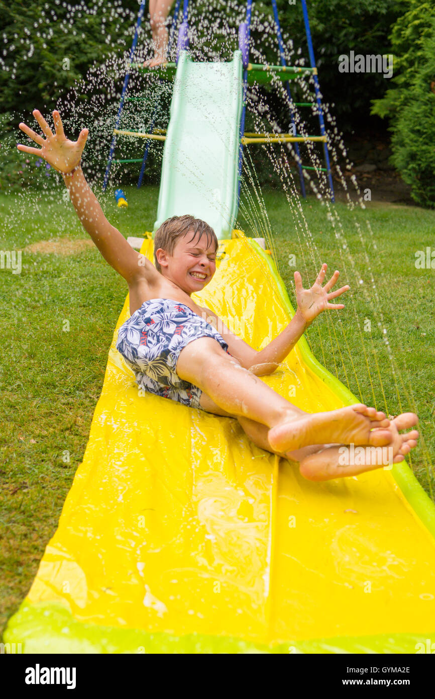 Boy, ten years old playing on water slide in back garden. UK. July