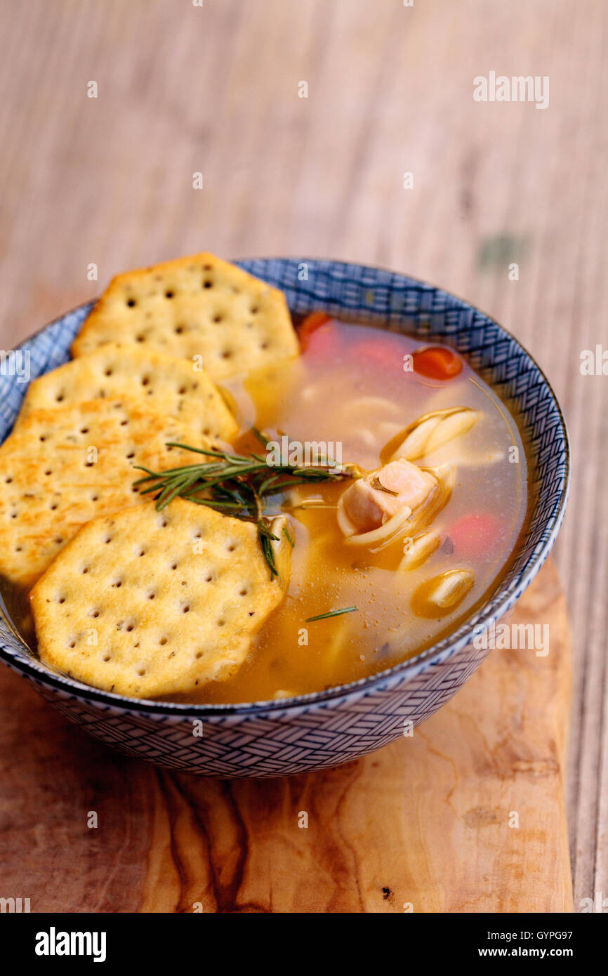 Chicken noodle soup in a blue and white bowl with crackers, all sitting