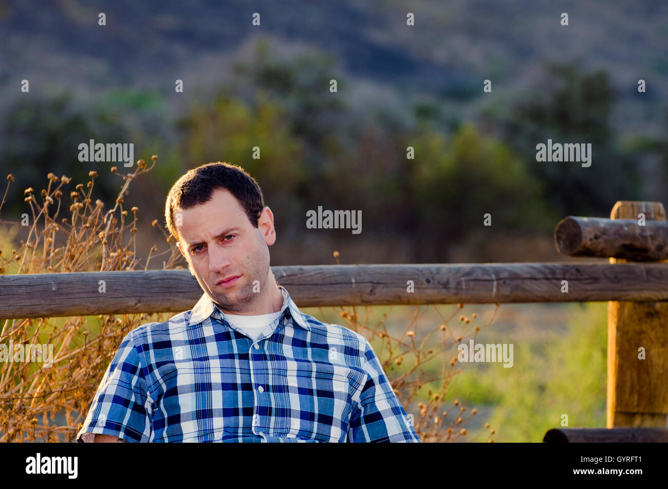 Man with a bored, indifferent expression slouching sitting in a field. Stock Photo