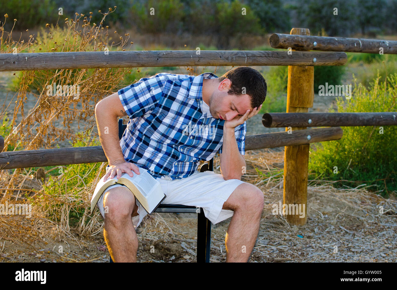Alone time outdoors man praying with his head in his hand and Bible in his lap. Stock Photo