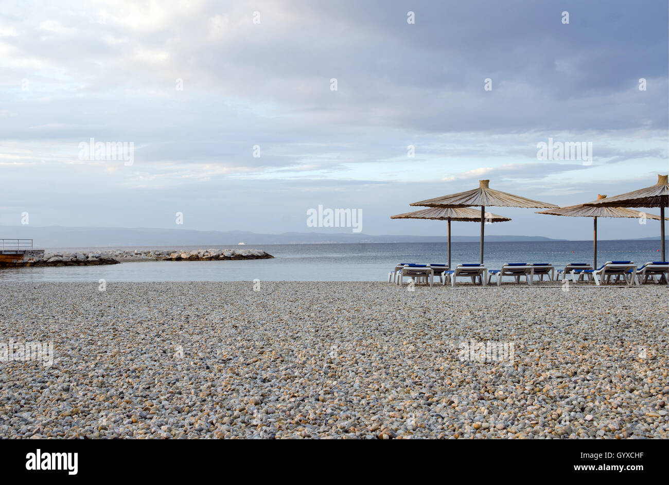 pebbled beach with lounge chairs and thatched umbrellas Stock Photo