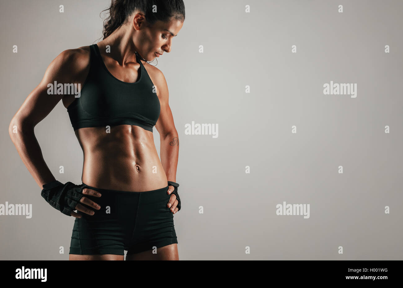 Tough woman with gloved hands on hips featuring tight abdominal muscles over gray background with copy space Stock Photo