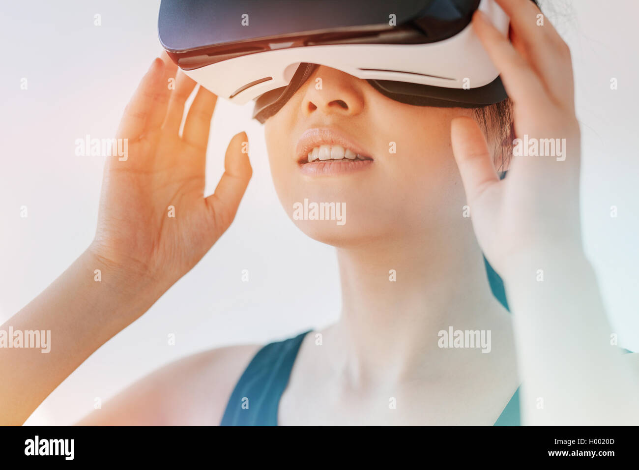 Close up shot of asian woman using the virtual reality headset and looking away. Female wearing VR goggles against grey backgrou Stock Photo