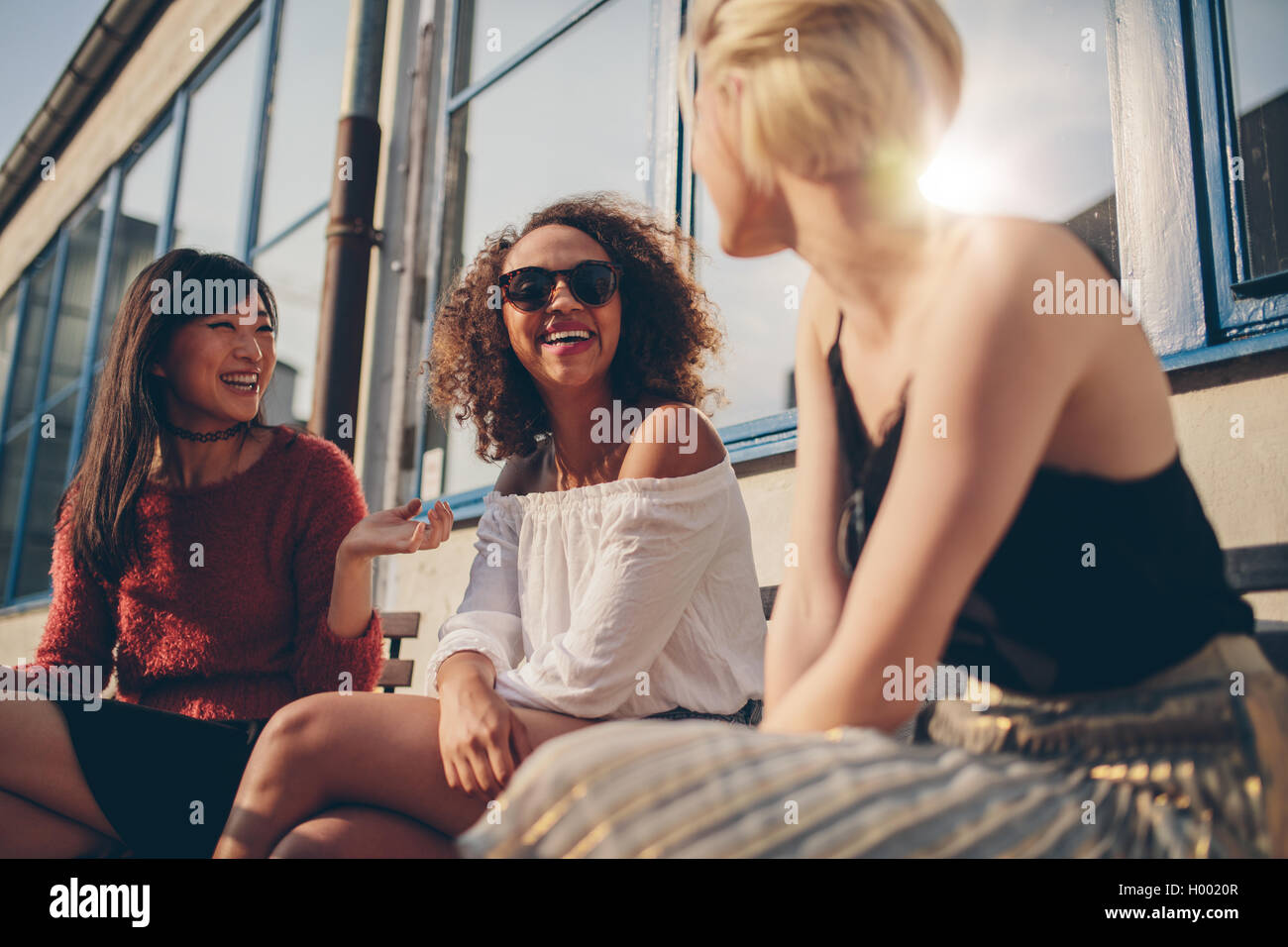 Three young women meeting at outdoor cafe chatting and enjoying. Group of female friends having fun while sitting in a terrace. Stock Photo