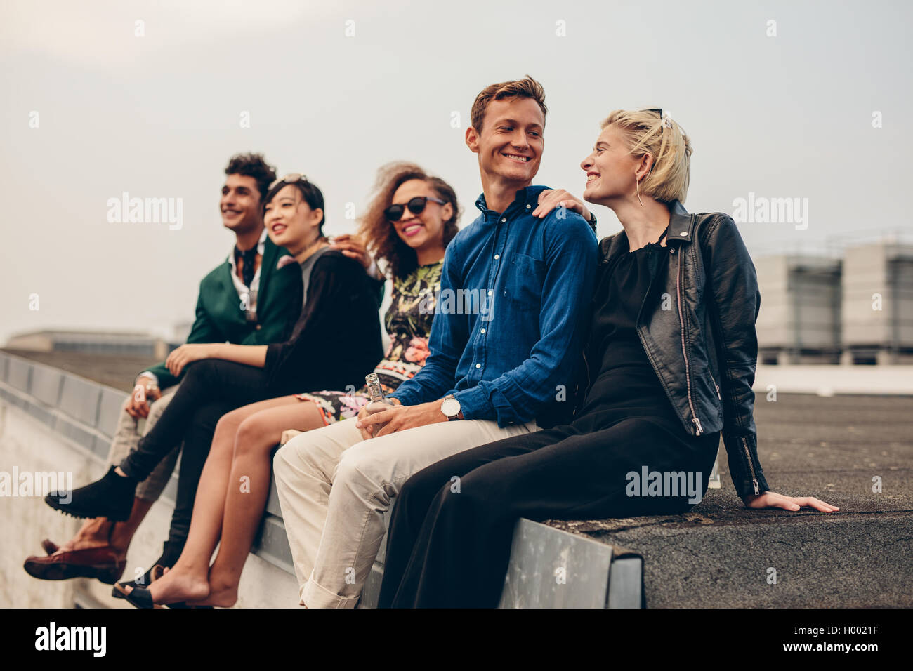Shot of young men and women sitting together on rooftop. Mixed race friends relaxing on terrace. Stock Photo