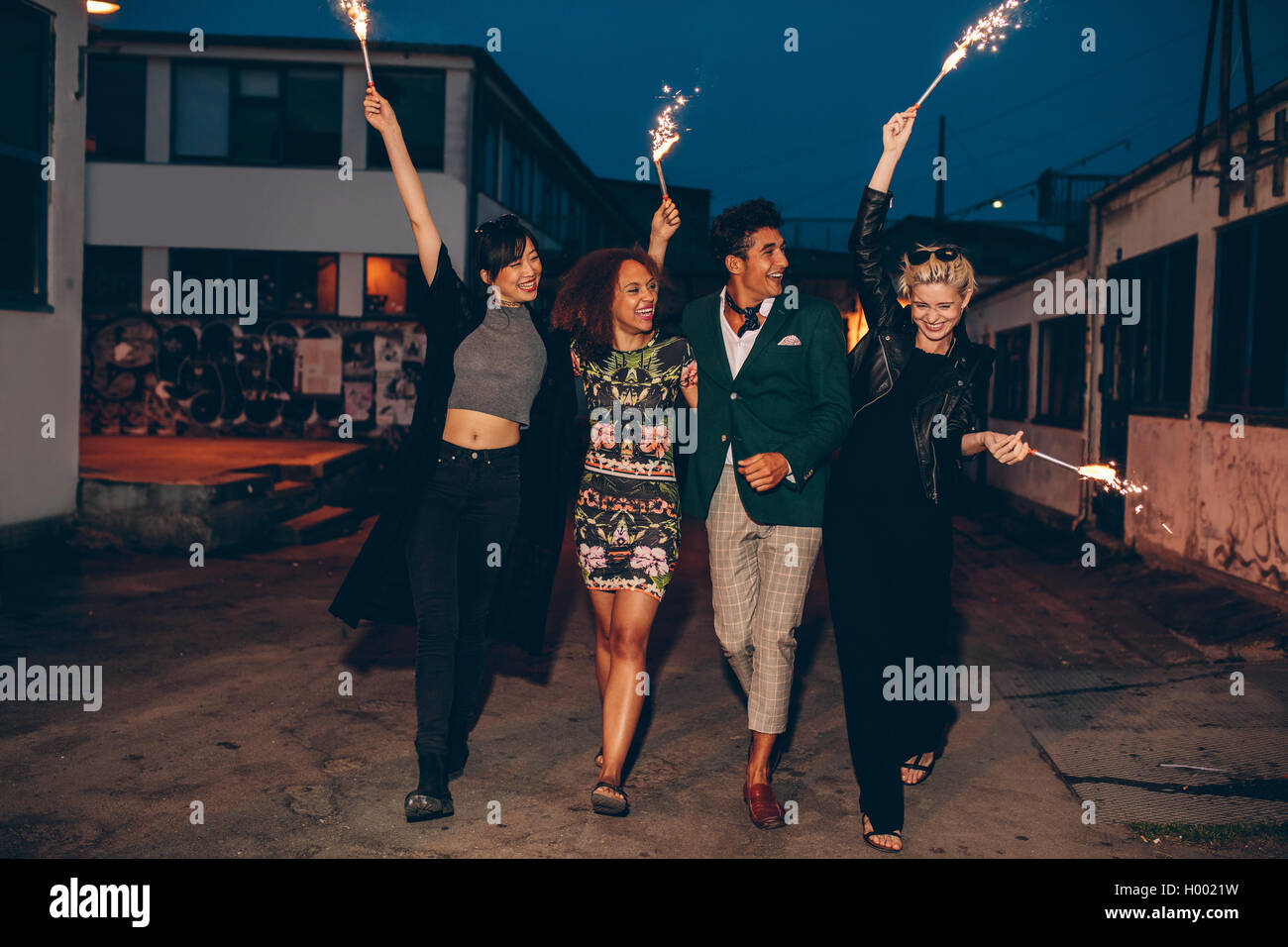 Full length shot of four young friends walking down the city street with fireworks and celebrating new years eve. Group of peopl Stock Photo