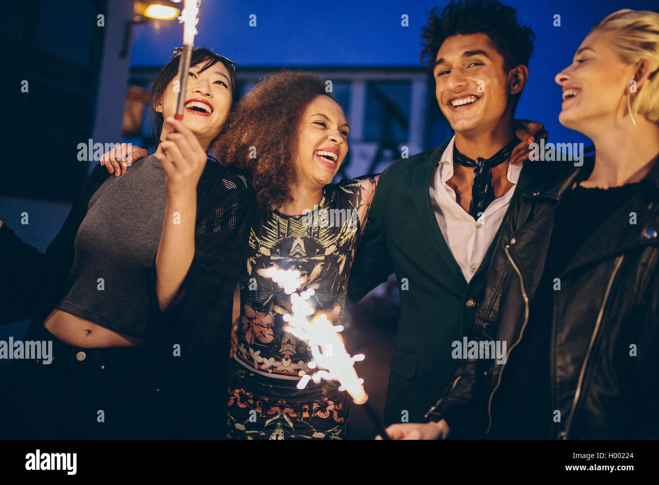 Shot of young man and women in city at night with fireworks. Group of friends enjoying with sparklers on road in evening. Stock Photo