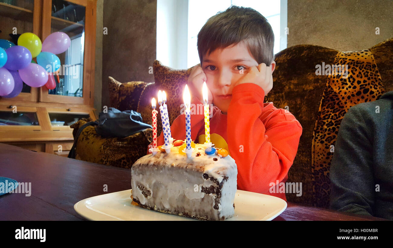 Geburtstagskind sitzt voller Vorfreude vor dem Geburtstagskuchen mit brennenden Kerzen, Deutschland | birthday boy sitting in fu Stock Photo