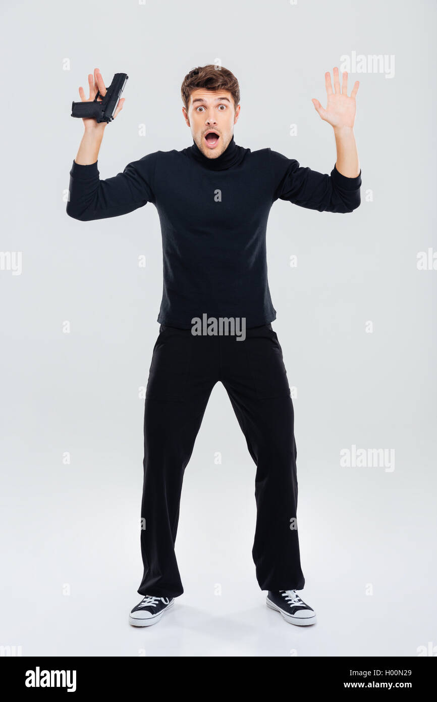 Full length of scared young man holding gun and standing with hands up Stock Photo