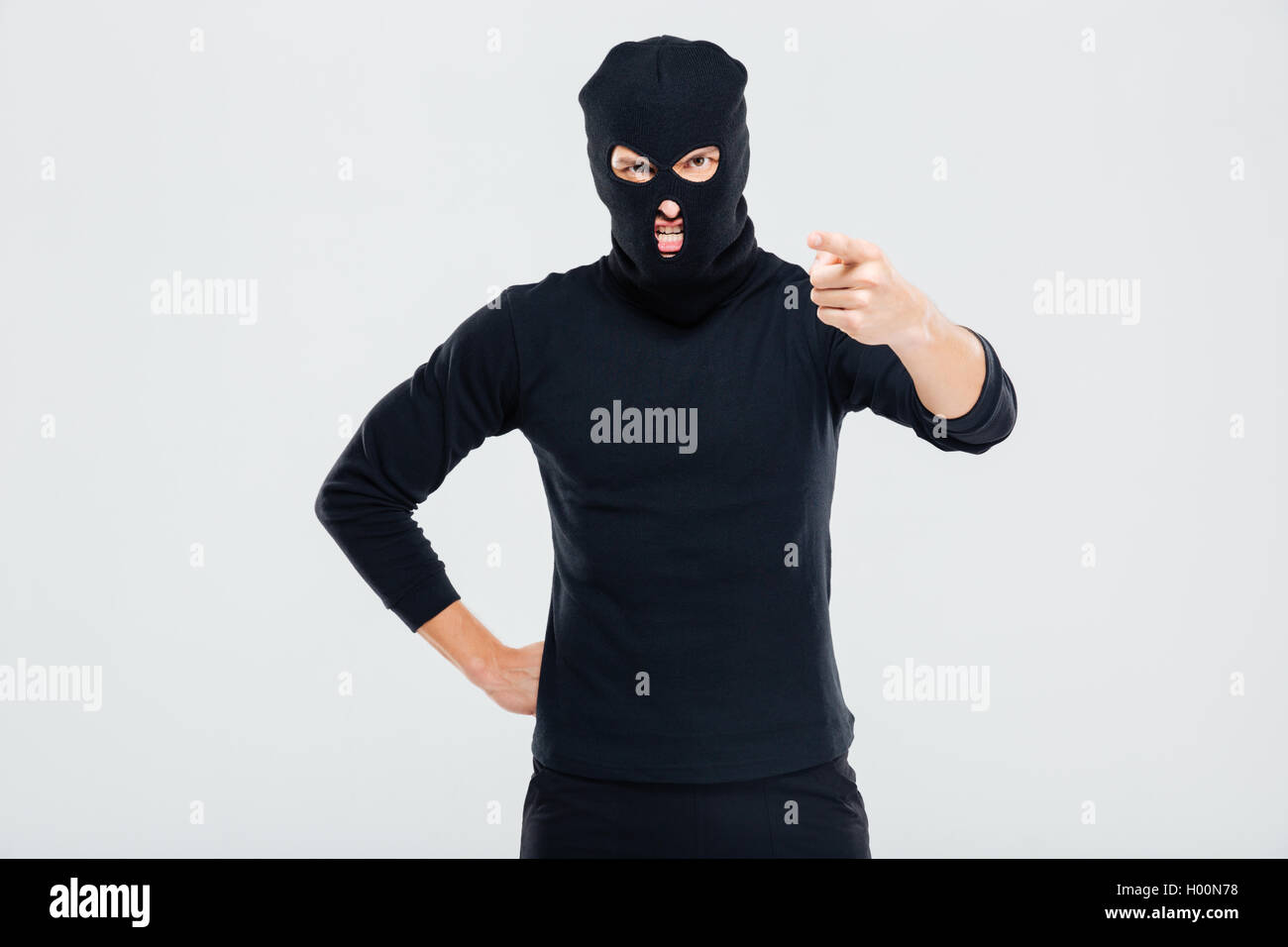 Mad irritated young man in balaclava standing and pointing on you Stock