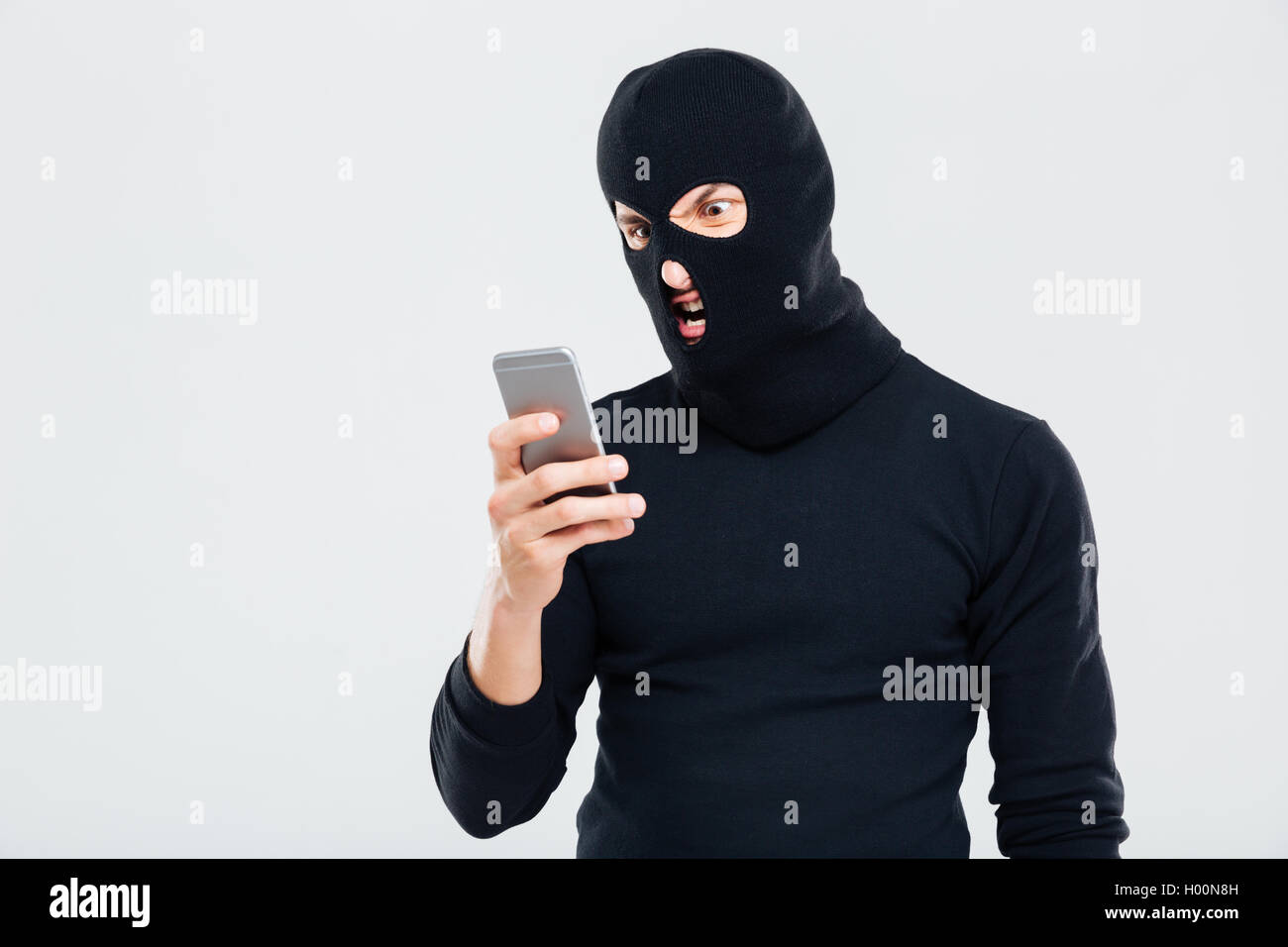 Angry young man in balaclava using cell phone Stock Photo