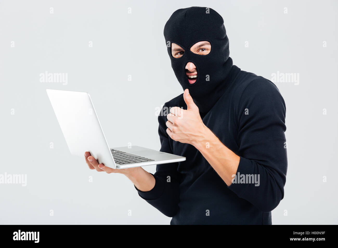 Man in balaclava using laptop and showing thumbs up Stock Photo Alamy