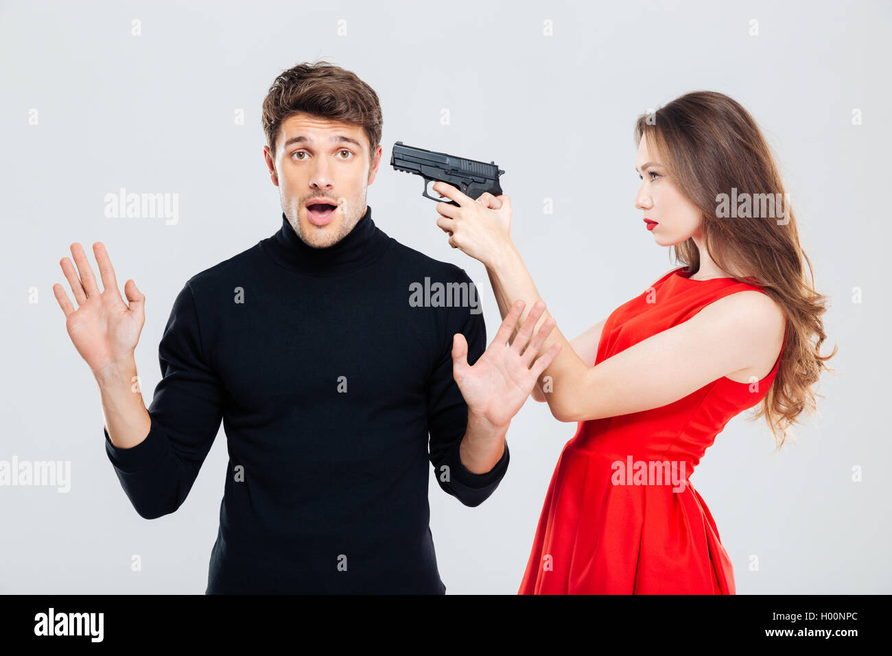 Beautiful young woman standing and threatening with gun to scared young man Stock Photo
