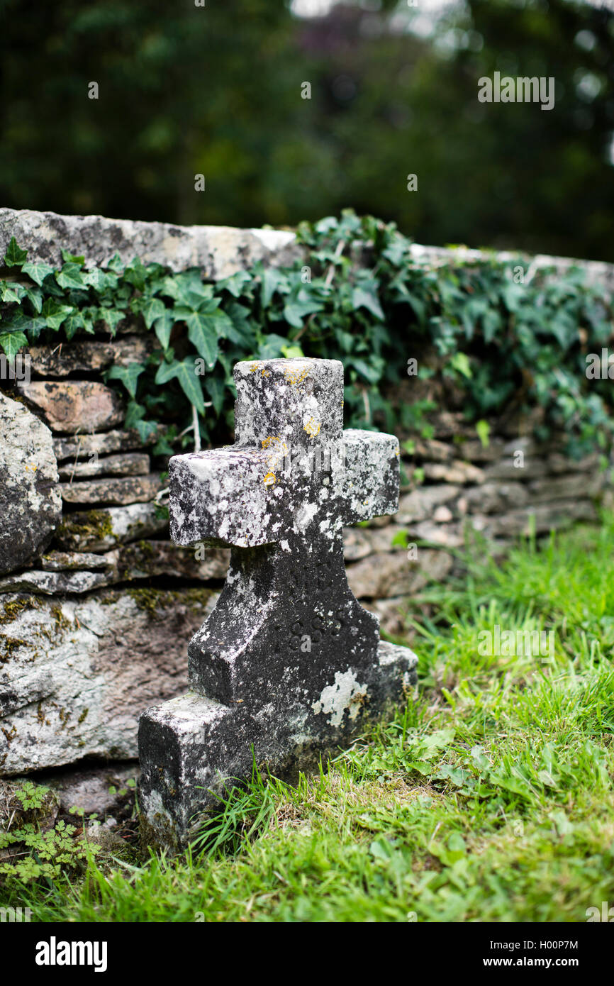 Weathered grave stone in the shape of a cross in a church yard. Stock Photo