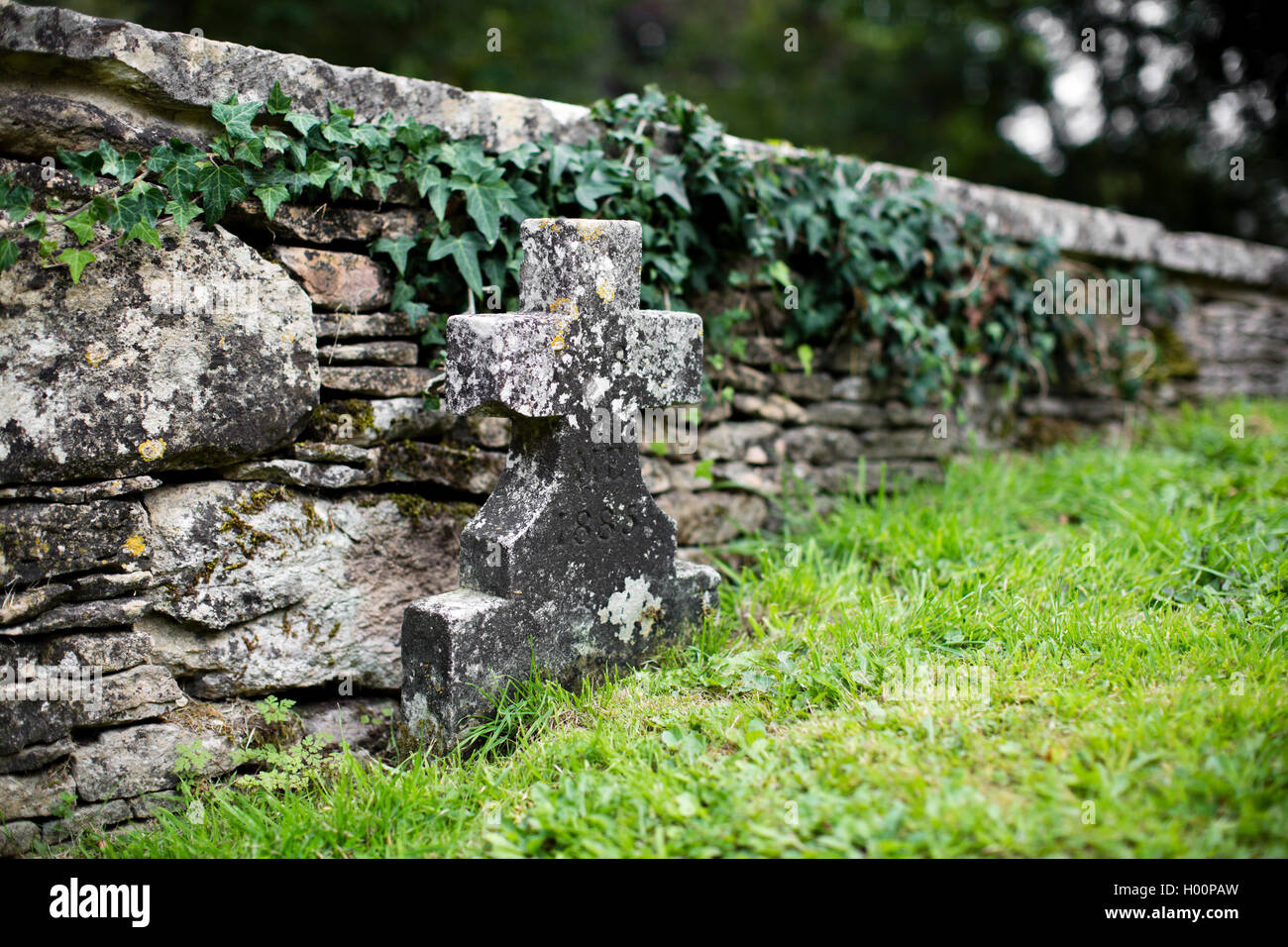 Weathered grave stone in the shape of a cross in a church yard. Stock Photo