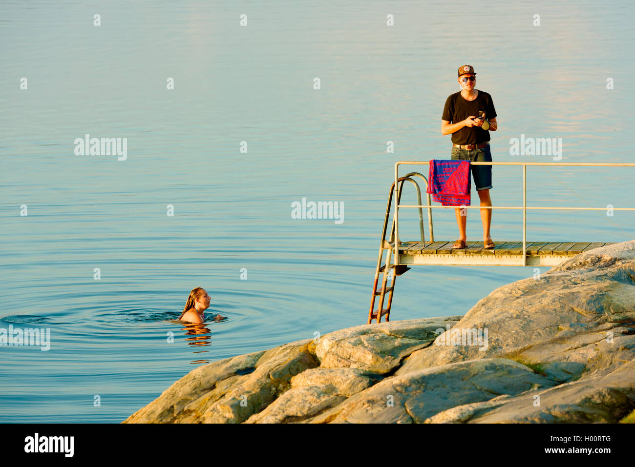 Marstrand, Sweden - September 8, 2016: Documentary of evening sea bathing in windless water. Female in water and male on pier wi Stock Photo