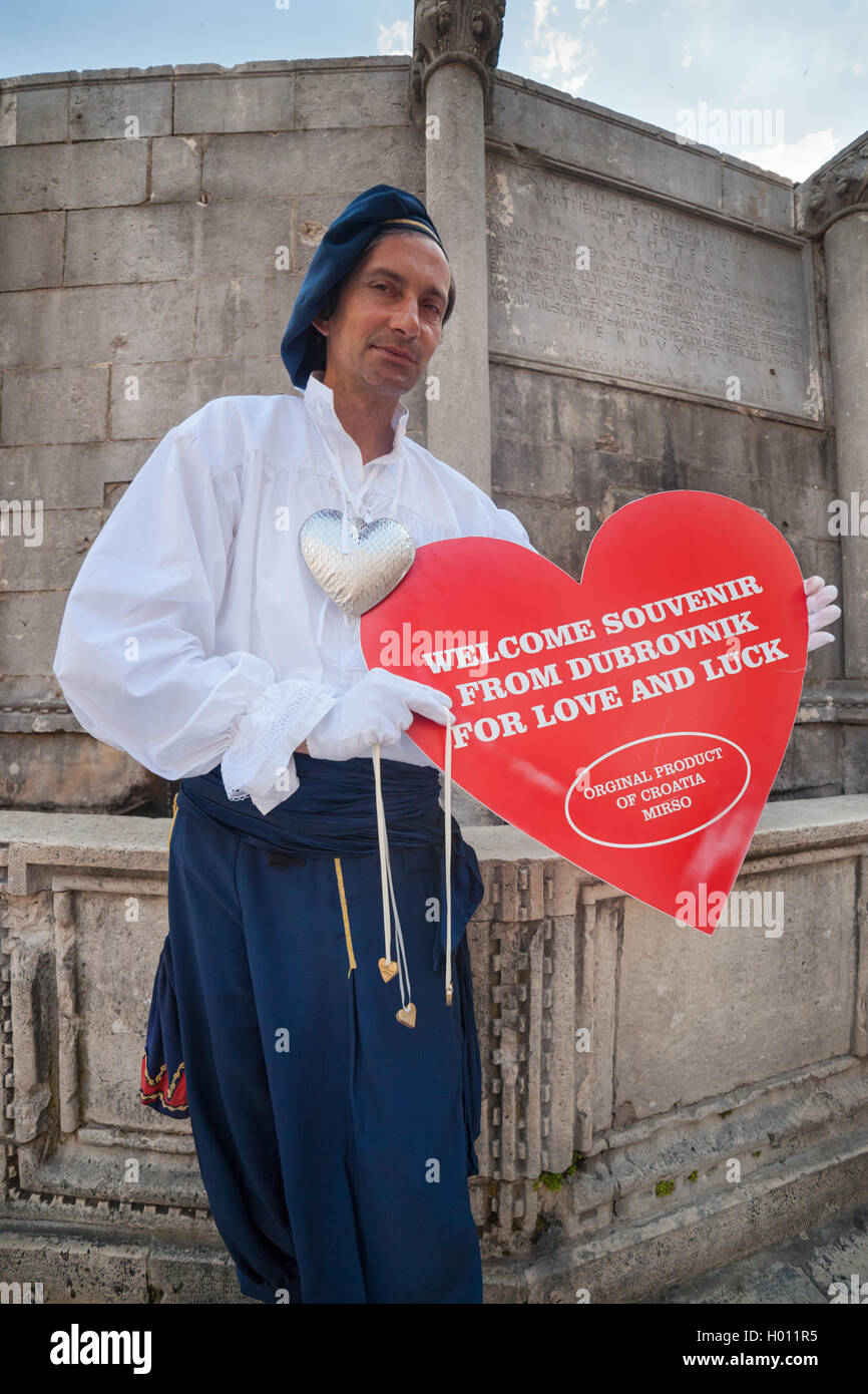 DUBROVNIK, CROATIA - MAY 27, 2014: Man wearing old traditional clothes holding big souvenir heart in front of Onofrio's fountain Stock Photo