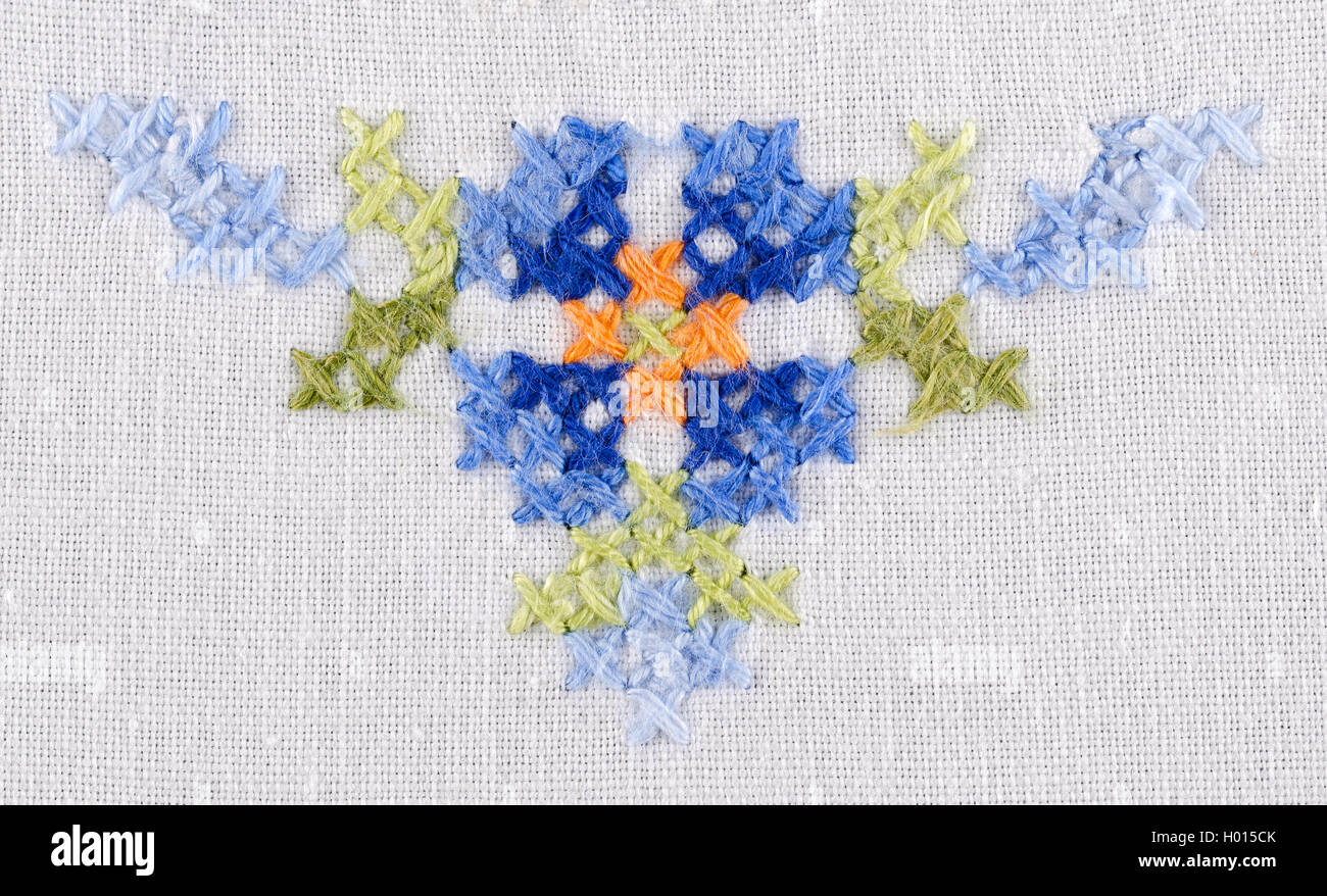 Blue flower triangle motif hand embroidery on white linen tablecloth.  Multicolored cross stich decoration with yarn. Stock Photo