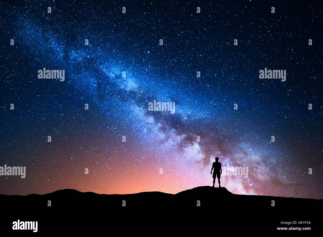 Milky Way. Beautiful night sky with stars and silhouette of a standing alone man on the mountain. Blue milky way with red light Stock Photo