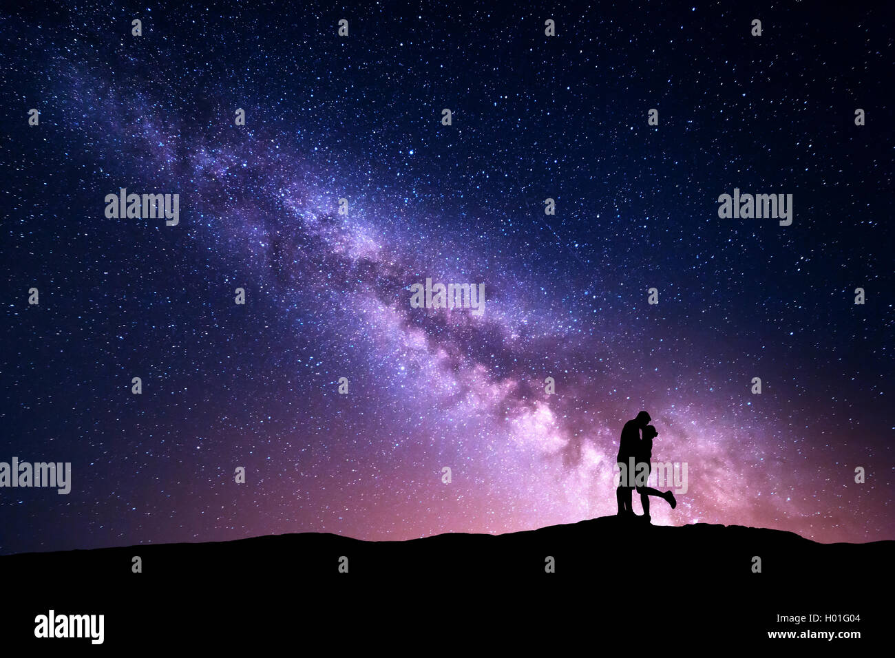 Milky Way. Night landscape with silhouettes of hugging and kissing man and woman on the mountain. Colorful sky with stars. Silho Stock Photo