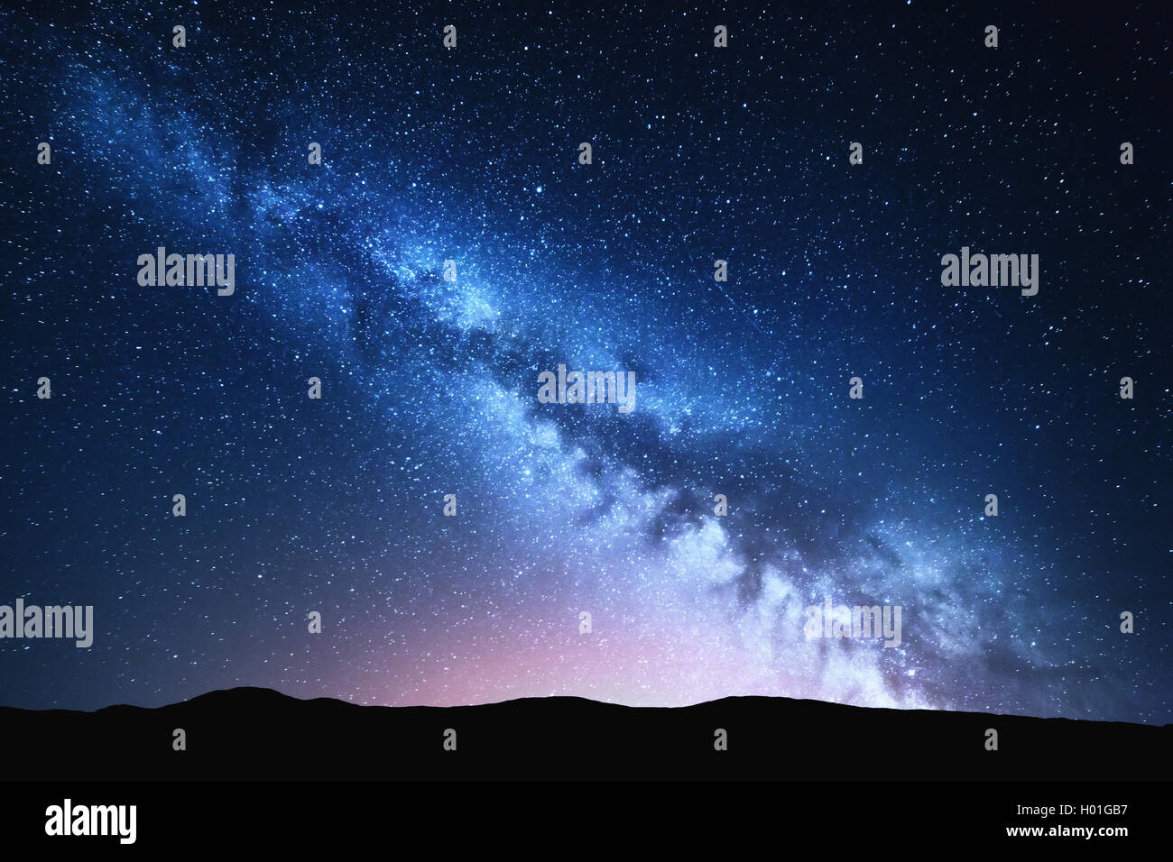 Milky Way and pink light at mountains. Night colorful landscape. Starry sky with hills at summer. Beautiful Universe. Space back Stock Photo
