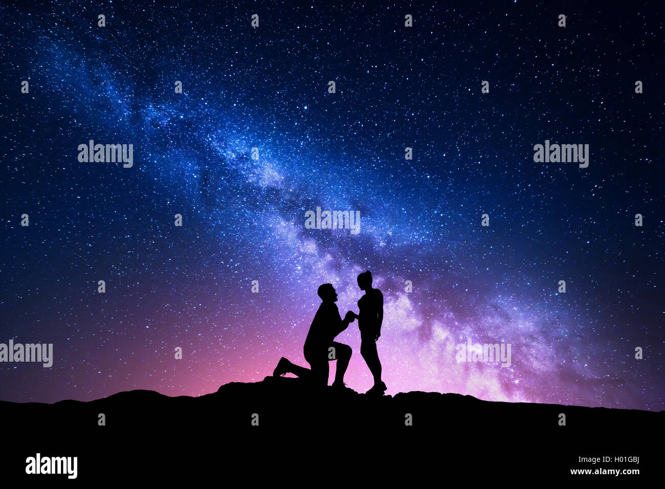 Milky Way. Night landscape with silhouettes of a man making marriage proposal to his girlfriend and starry sky. Silhouette of lo Stock Photo