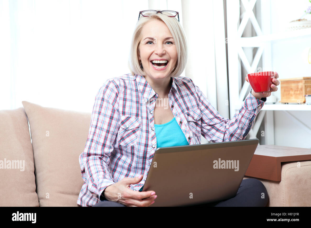Woman sitting on sofa and uses a laptop Stock Photo - Alamy