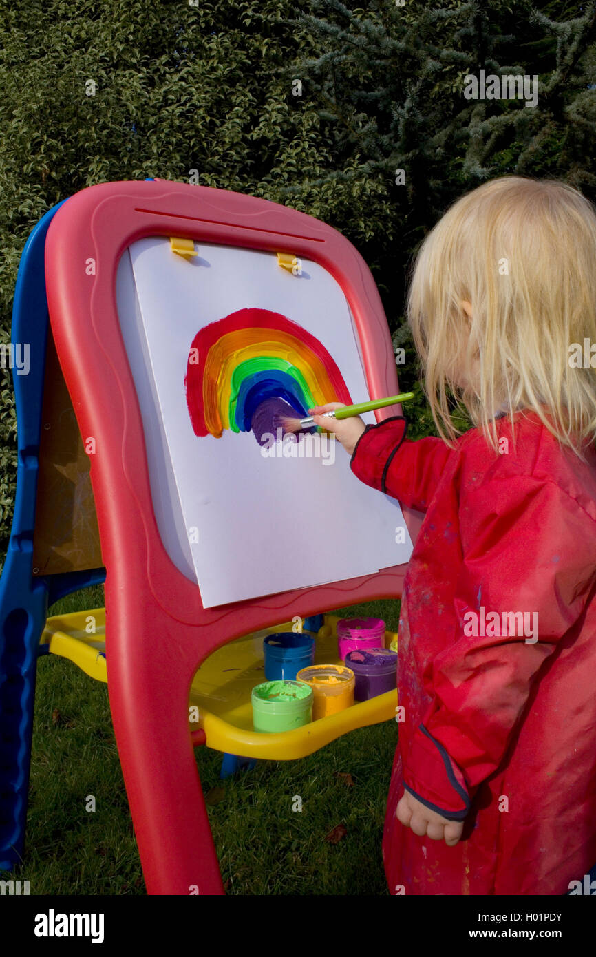 School girl painting rainbow on an easel outdoors Stock Photo