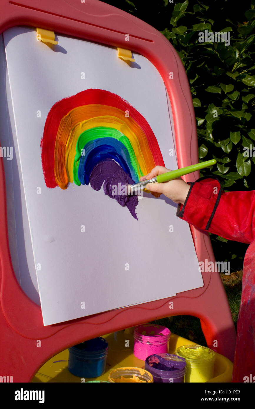 School girl painting a rainbow on an easel outdoors Stock Photo