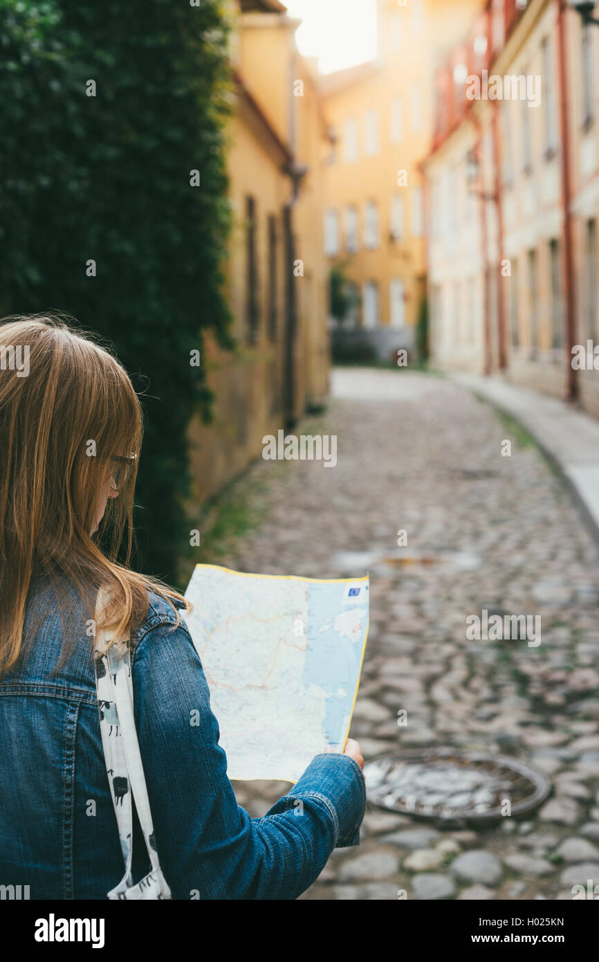 Young female tourist with paper map looking for a way on a narrow scenic street Stock Photo