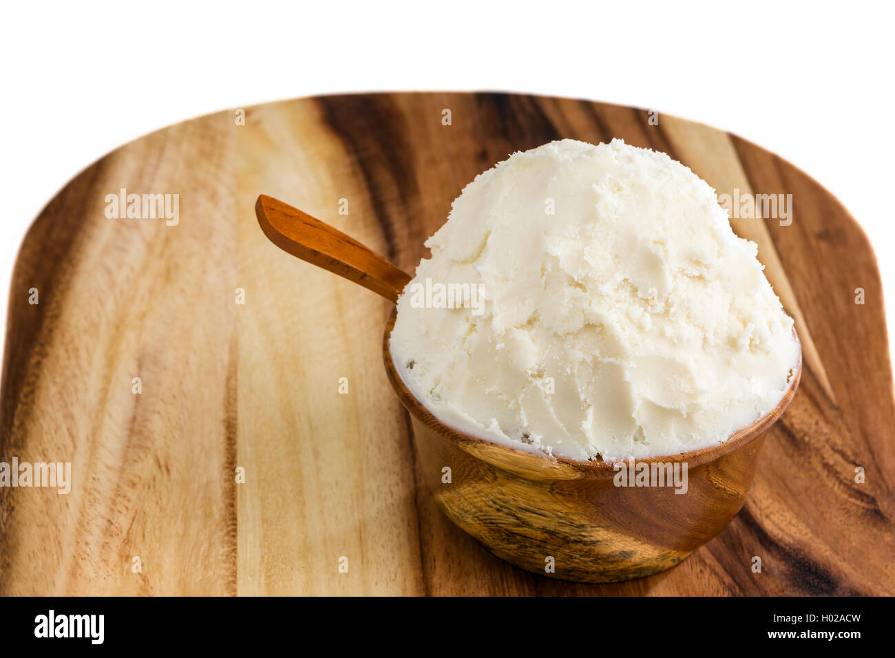 Unrefined, organic Shea butter in the wooden bowl with the spoon, stands on the wooden board, clean white background. Stock Photo
