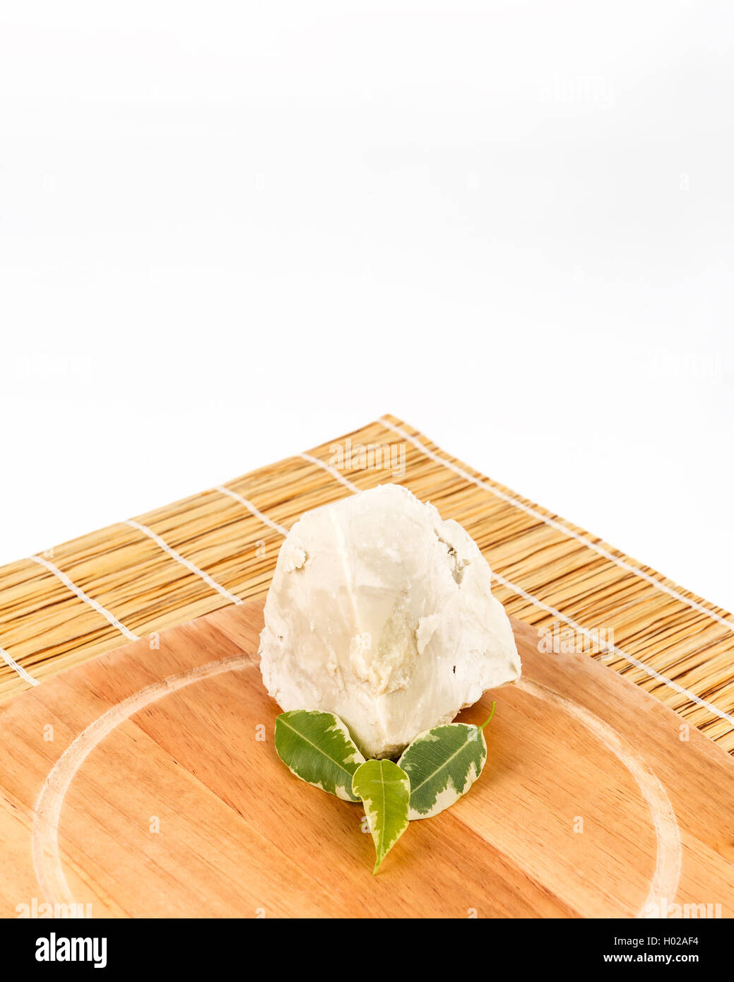 Unrefined, organic Shea butter with green leaves laying on the wooden board which is laying on the straw mat, clean white backgr Stock Photo