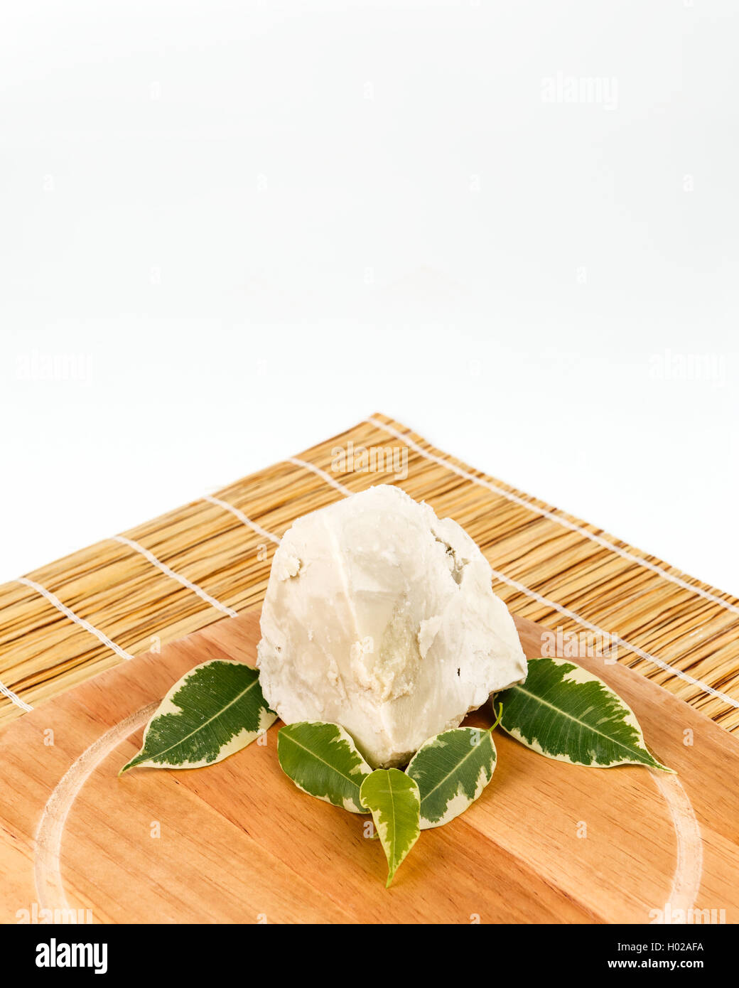 Unrefined, organic Shea butter with green leaves laying on the wooden board which is laying on the straw mat. Stock Photo