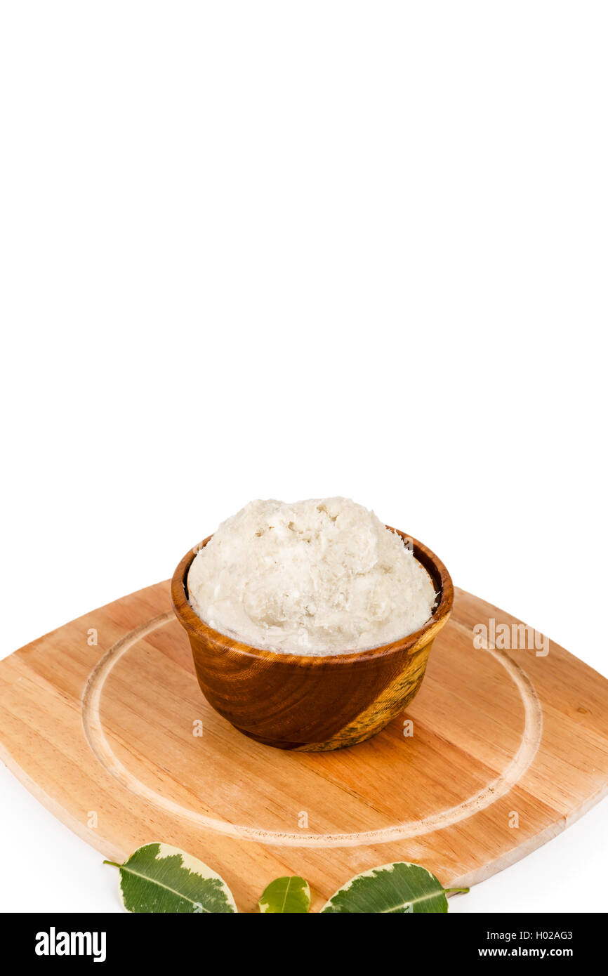 Unrefined, organic Shea butter in the wooden bowl and with green leaves stands on the wooden board, clean white background. Stock Photo