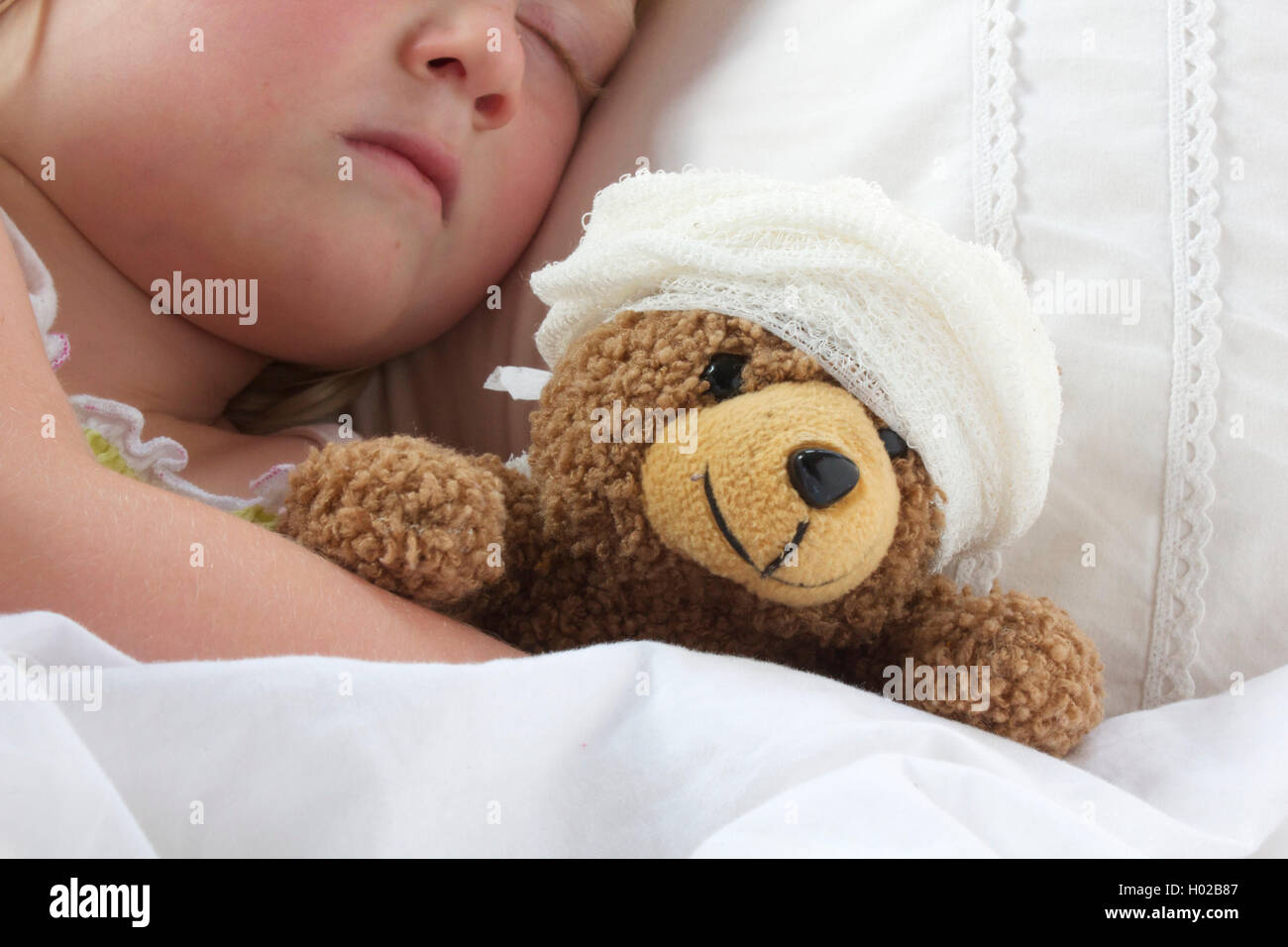 A young girl poorly in bad cuddling her teddy who also feels poorly