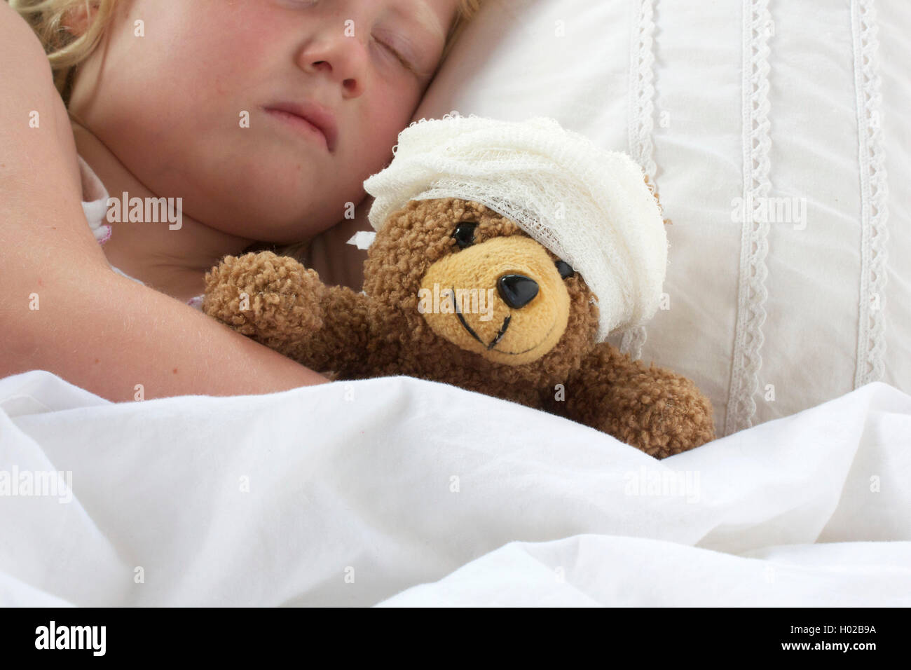A young girl poorly in bed cuddling her teddy who also feels poorly. Stock Photo