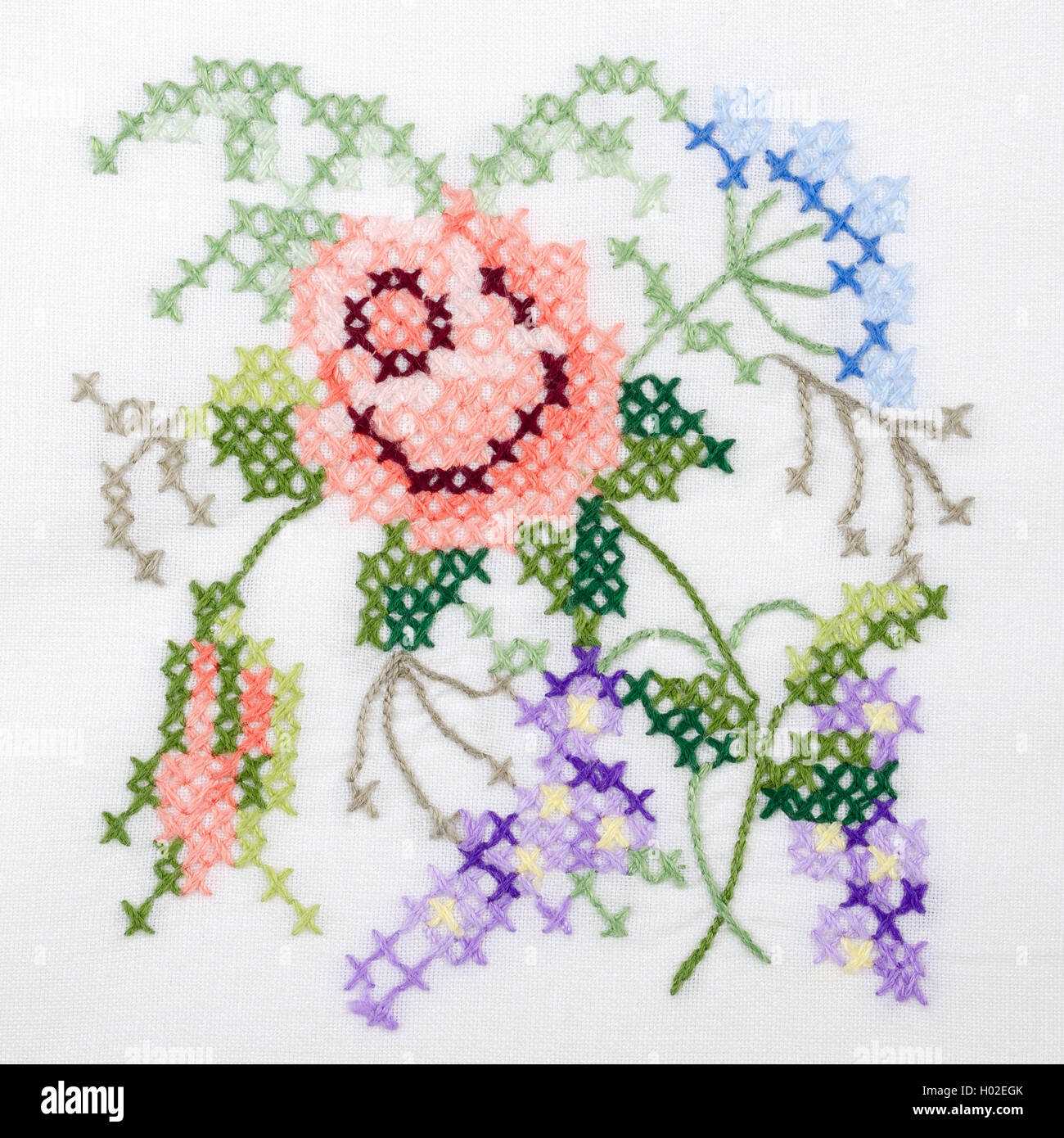 Flowers motif hand embroidery on white linen tablecloth.  Multicolored cross stich decoration with yarn. Handicraft. Macro photo Stock Photo