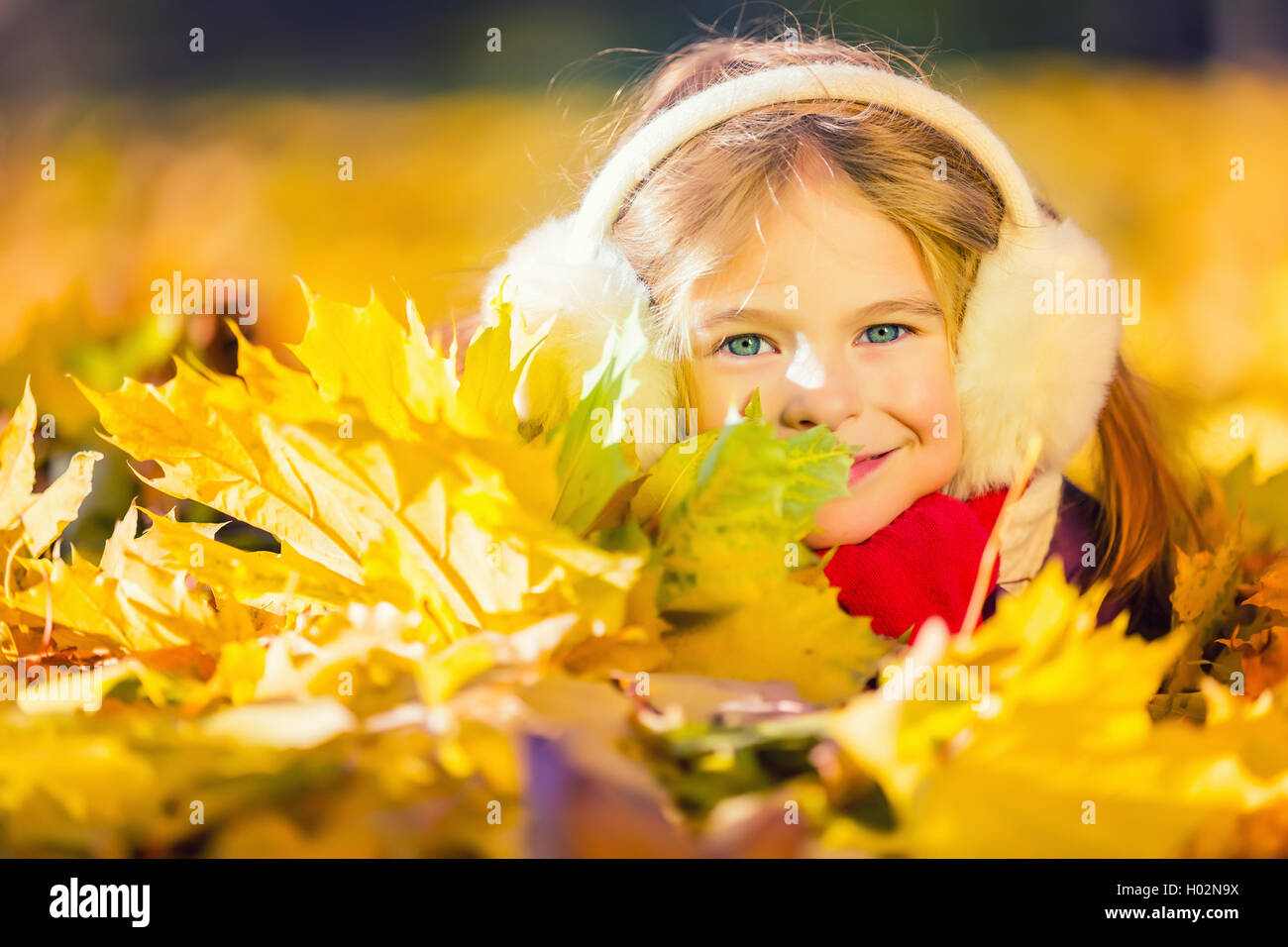 Little girl in earflaps playing with autumn leaves Stock Photo - Alamy