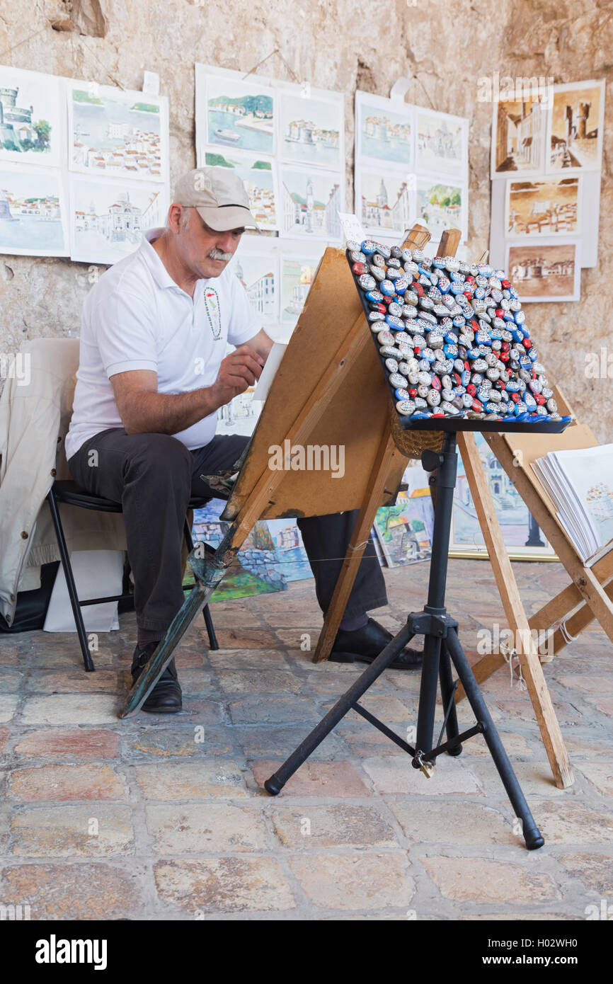 DUBROVNIK, CROATIA - MAY 26, 2014: Elderly painter drawing water color paintings at street. Stock Photo