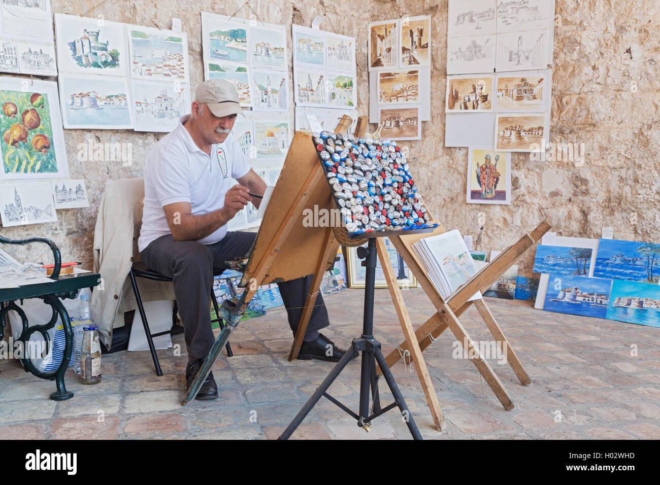 DUBROVNIK, CROATIA - MAY 26, 2014: Elderly painter drawing water color paintings at street. Stock Photo