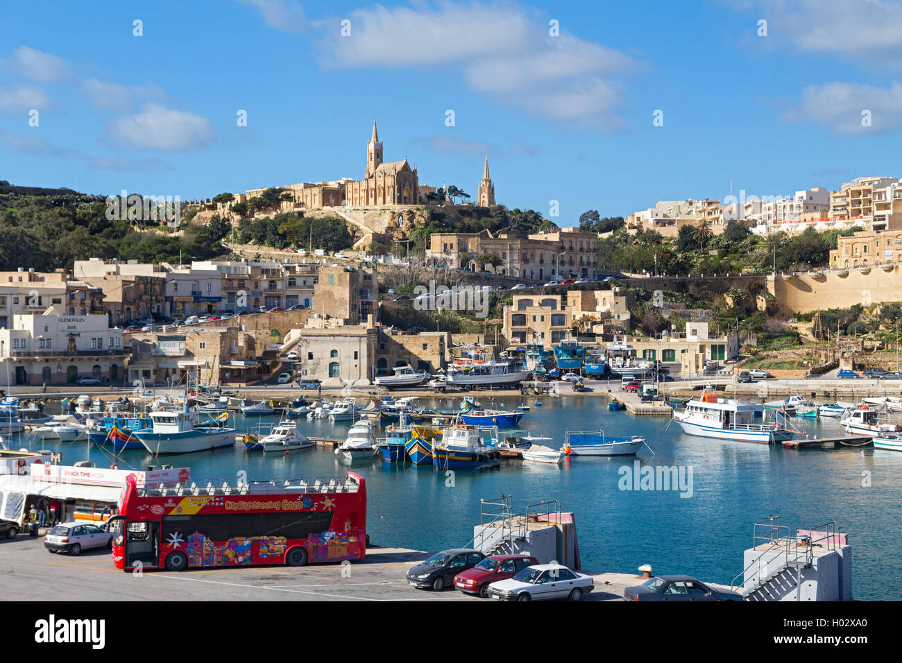 MGARR, MALTA - JANUARY 13, 2015: Mgarr harbour with view of church Our Lady of Lourdes on top of the hill, Gozo island. Stock Photo