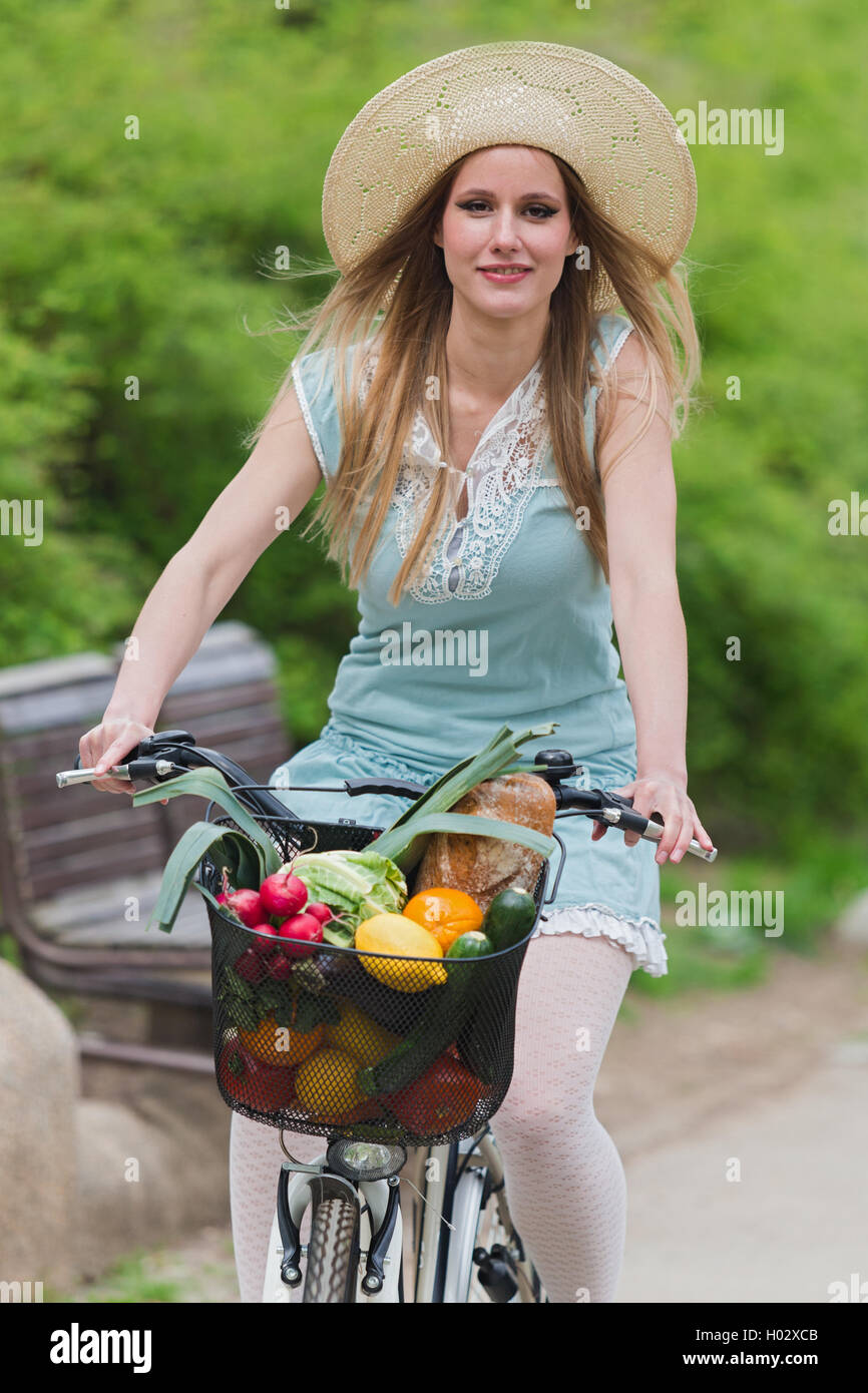 Attractive blonde woman with straw hat riding a bike with basket full of groceries Stock Photo