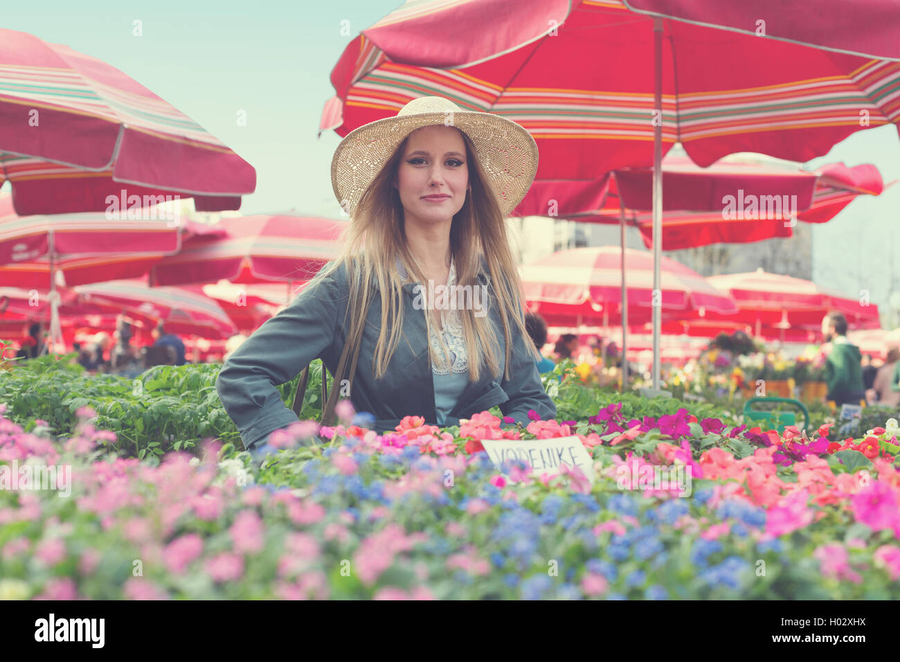 Attractive blonde girl with straw hat posing on flower marketplace ...
