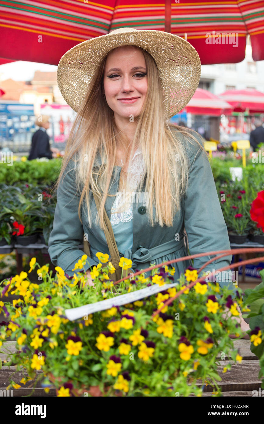 Attractive blonde woman with straw hat posing on flower marketplace ...