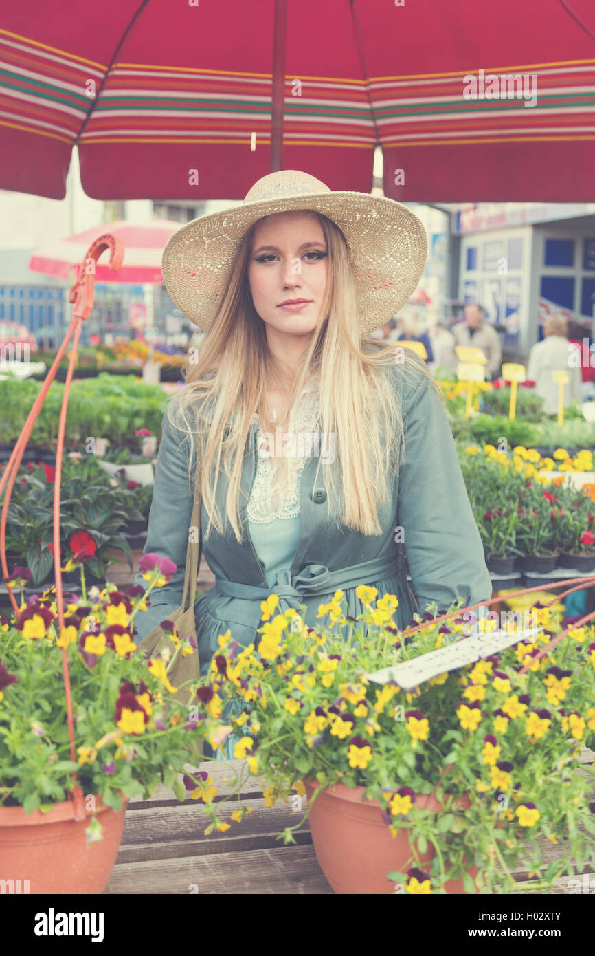 Attractive blonde girl with straw hat posing on flower marketplace ...