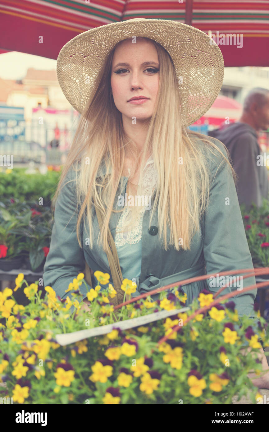 Attractive blonde girl with straw hat posing on flower marketplace ...