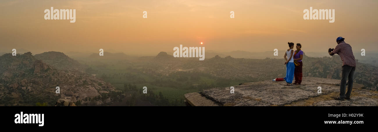 HAMPI, INDIA - 03 FEBRUARY 2015: Two female tourists being photographed by man on hilltop in sunrise Stock Photo