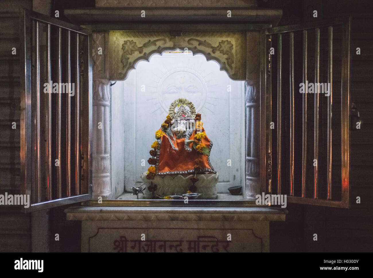 Small Ganesh sculpture in mini street temple decorated with flowers. Stock Photo