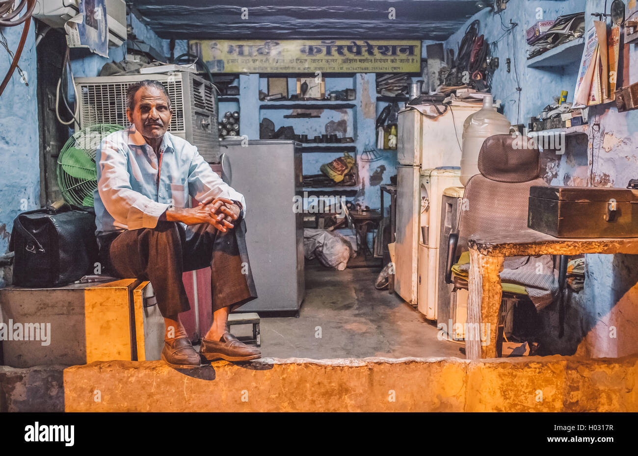 JODHPUR, INDIA - 10 FEBRUARY 2015: Elderly electrician sits on fridge before closing refrigerator service shop. Post-processed w Stock Photo