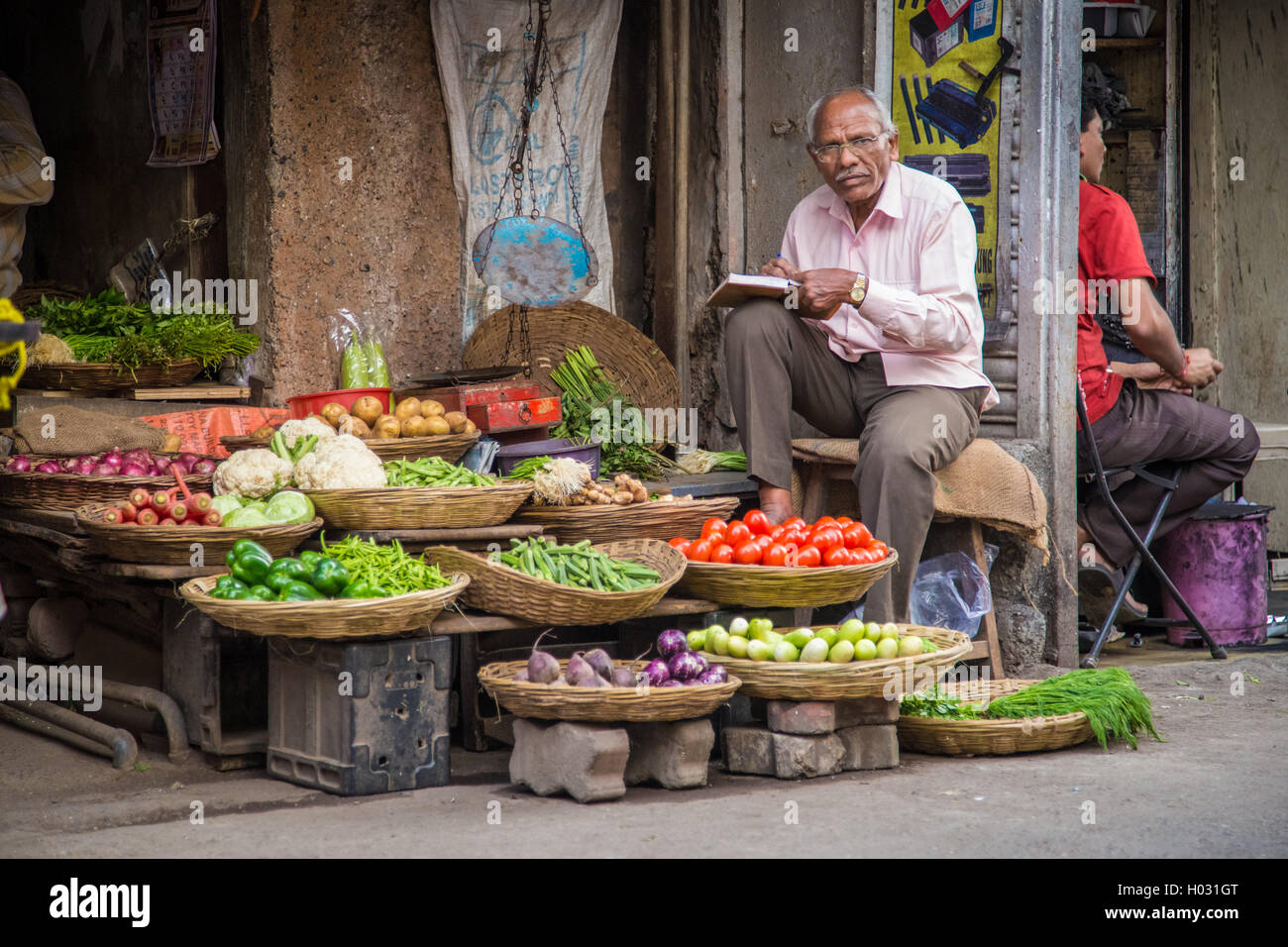 MUMBAI, INDIA - 17 JANUARY 2015: Elderly Indian businessman waits for customers in front of grocery store in market street. Stock Photo